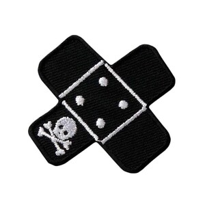 May include: A black embroidered patch shaped like an adhesive bandage with rounded corners. The center features a white stitched square with four white dots arranged like a die, and a white skull and crossbones icon on the lower left side.