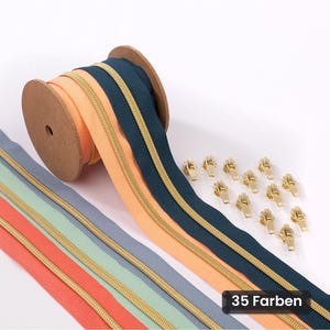 Op de afbeelding: Een spoel met donkerblauw ritsband met gouden tanden, vergezeld van losse stroken perzik, lichtblauw, mintgroen en koraalkleurig ritsband, samen met twaalf losse gouden ritsschuivers. Een zwart label toont de tekst 35 Farben.