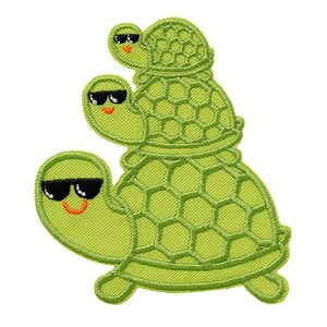 Pode incluir: Um emblema bordado com três tartarugas verde-limão empilhadas verticalmente. Cada tartaruga tem um padrão de carapaça texturizado, uma pequena boca laranja e óculos de sol pretos. As tartarugas formam uma torre com a maior na base.