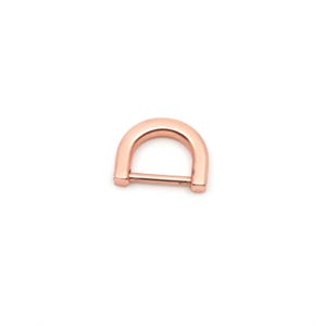 Könnte beinhalten: Ein D-Ring aus roségoldfarbenem Metall mit einer glatten, polierten Oberfläche. Der D-Ring besteht aus einem gebogenen oberen Teil und einem geraden horizontalen Steg an der Unterseite, was eine halbkreisförmige Form für verschiedene Bastelprojekte ergibt.