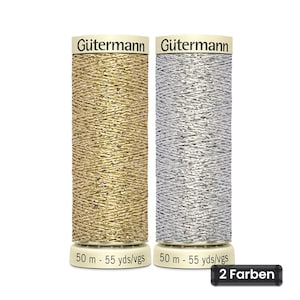 Op de afbeelding: Twee klossen Gütermann metallic garen, één goud en één zilver, elk gelabeld 50 m - 55 yds/vgs. De cilindrische klossen hebben een textuurrijke, glinsterende afwerking en staan naast elkaar met de merknaam bovenaan op de klossen gedrukt.