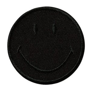 Op de afbeelding: Een ronde zwarte geborduurde patch met een gestikt smiley-gezicht. De patch heeft een effen zwarte achtergrond met twee verticale gestikte lijnen voor de ogen en een gebogen gestikte lijn die een brede, omhoog gekrulde mond vormt.
