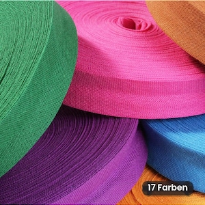 Könnte beinhalten: Mehrere Rollen gewebtes Baumwoll-Köperband in leuchtenden Farben wie Grün, Pink, Lila, Blau und Orange. Der Stoff weist ein ausgeprägtes diagonales Fischgrätenmuster auf. Ein kleines schwarzes Etikett zeigt den Text 17 Farben.