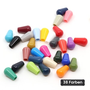 Pode incluir: Uma coleção de pequenas tampas cónicas de plástico numa grande variedade de cores sólidas, incluindo vermelho, azul, amarelo, verde, rosa, preto, branco e laranja. Uma etiqueta retangular preta no canto inferior direito exibe o texto 38 Farben.