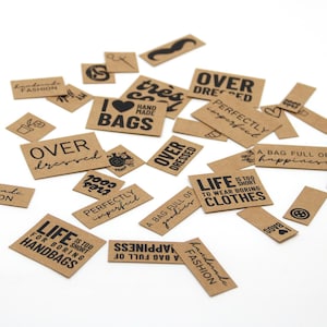 Può includere: Una collezione di etichette rettangolari in carta kraft marrone con varie frasi e icone stampate in nero, tra cui "Life is too short to wear boring clothes", "Over dressed", "Handmade fashion", "Perfectly imperfect" e "I love handmade bags".