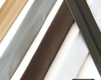May include: Several strips of textured material arranged diagonally in various colours including tan, light grey, dark brown, olive green, and silver. A small black rectangular label in the bottom right corner displays the text 9 Farben.