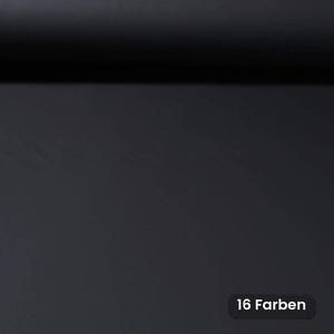 Op de afbeelding: Een effen zwarte stofrol met een gladde, matte textuur. In de rechterbenedenhoek bevindt zich een klein zwart rechthoekig label met de witte tekst 16 Farben, wat de beschikbaarheid van zestien verschillende kleuropties voor dit materiaal aangeeft.