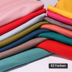 Könnte beinhalten: Eine Sammlung gefalteter Stoffmuster in verschiedenen Farben, darunter Rosa, Rot, Hellgrau, Olivgrün, Dunkelblau, Braun, Türkis, Gelb und Magenta. Ein schwarzes rechteckiges Etikett in der unteren rechten Ecke zeigt den Text 62 Farben.