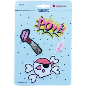 Può includere: Un set di quattro toppe ricamate su un cartoncino azzurro a pois, con le etichette BIPP DESIGN e PATCHES. Le toppe includono una nuvoletta da fumetto POW! rosa e gialla, un rossetto, un fulmine rosa e un teschio con una bandana rosa.