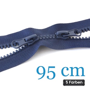 Könnte beinhalten: Ein dunkelblauer Kunststoffreißverschluss mit zwei passenden Schiebern auf einem Stoffband. Der Text 95 cm ist in Blau gedruckt, und ein kleines schwarzes rechteckiges Etikett zeigt den Text 5 Farben, was eine Länge von 95 cm angibt.