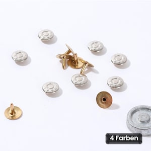 Puede incluir: Un conjunto de botones metálicos para vaqueros con una parte superior circular plateada con un patrón de estrellas y un poste de color latón. Se muestra un botón desde el reverso y una base circular plateada. El texto dice 4 Farben.