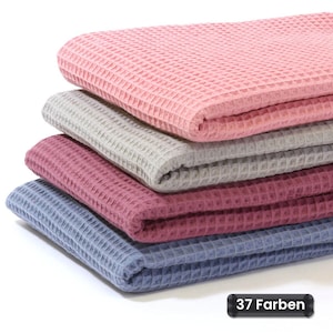 Könnte beinhalten: Ein Stapel aus vier gefalteten Stoffstücken mit Waffelstruktur in den Farben Rosa, Hellgrau, Dunkelrosa und Blau. Der Stoff weist durchgehend ein ausgeprägtes gitterartiges Muster auf. Ein kleines schwarzes rechteckiges Etikett zeigt den Text 37 Farben.