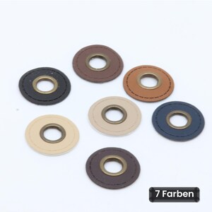Könnte beinhalten: Sieben kreisförmige Kunstleder-Patches in verschiedenen Farben wie Schwarz, Braun, Beige und Marineblau. Jeder Patch verfügt über eine zentrale, bronzefarbene Metallöse und abgesteppte Ränder. Der Text 7 Farben ist unten rechts zu sehen.