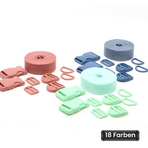 Op de afbeelding: Een set knutselbenodigdheden met drie rollen nylon band in oudroze, mintgroen en leiblauw. Elke rol wordt vergezeld door bijpassende plastic gespen, schuifgespen en D-ringen. De tekst 18 Farben is zichtbaar op de afbeelding.