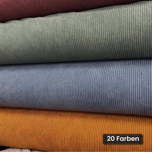 Puede incluir: Una pila de cuatro rollos de tela de pana doblados en tonos burdeos intenso, verde salvia, azul polvoriento y amarillo mostaza. Cada pieza presenta una textura acanalada vertical. Una etiqueta negra muestra el texto 20 Farben.