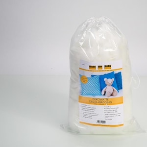 Può includere: Un sacchetto di plastica trasparente riempito con imbottitura in fibra sintetica bianca. L'etichetta presenta il logo del marchio Vlieseline, immagini di un cuscino blu a pois e un orsacchiotto, e il testo DEKOWATTE DECO-WADDING per imbottiture.