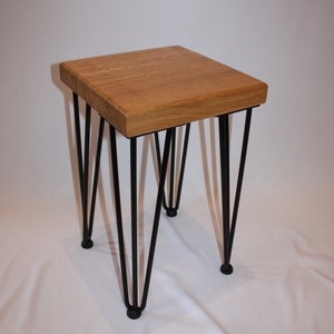 May include: A small wooden stool with a square top and black hairpin legs.