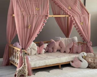 May include: A wooden canopy bed with pink tulle curtains and decorative butterfly accents. The bed is furnished with butterfly-shaped pillows, a giraffe plush toy, and a swan-shaped pillow. The bed sits on a white fluffy rug.
