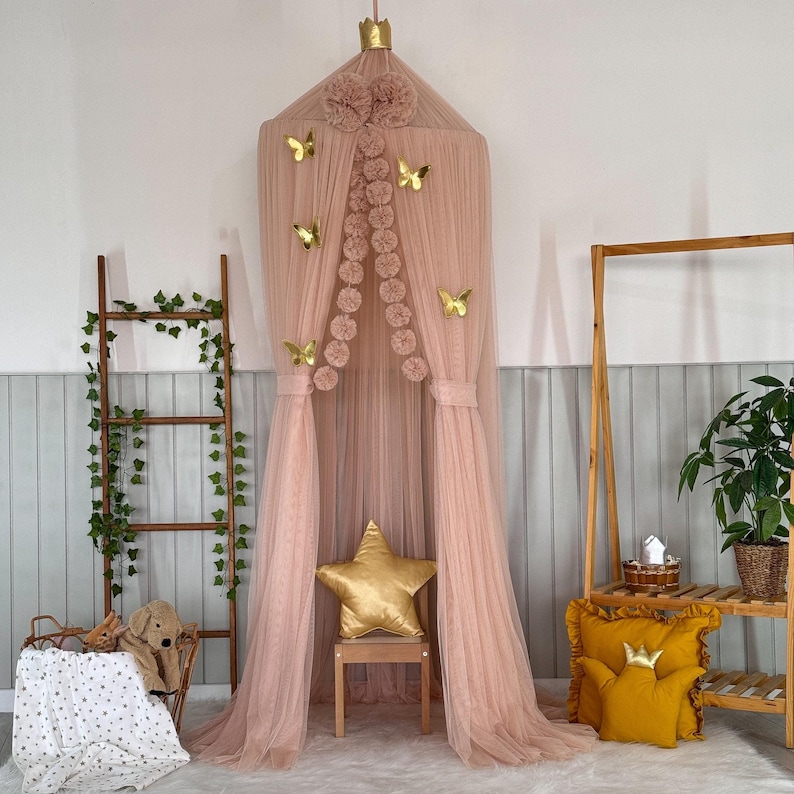 May include: A pink tulle canopy with gold butterfly and star decorations. The canopy is set up in a room with a wooden ladder and a shelf unit.