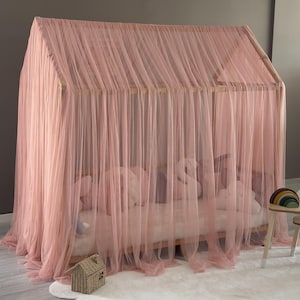 May include: A pink canopy bed with a wooden frame and sheer, flowing fabric. The bed is decorated with pillows and a small decorative house. The bed is on a white rug.