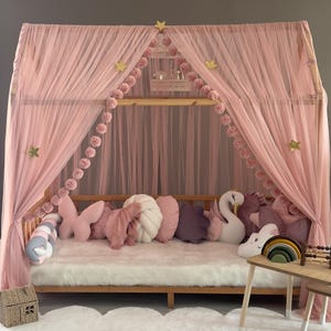 May include: A pink canopy bed with sheer curtains and a wooden frame. The bed is decorated with pink pillows, including butterfly and cloud shapes. A white rug and decorative stars complete the whimsical design.