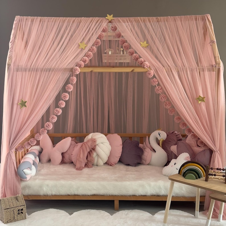 May include: A pink canopy bed with sheer curtains and a wooden frame. The bed is decorated with pink pillows, including butterfly and cloud shapes. A white rug and decorative stars complete the whimsical design.