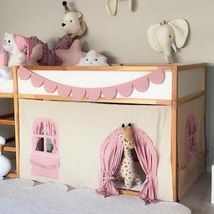 May include: A wooden bed frame with a white and pink scalloped trim and a beige fabric canopy. The canopy has pink window and door cutouts with ruffled edges. A stuffed giraffe is visible in the doorway.