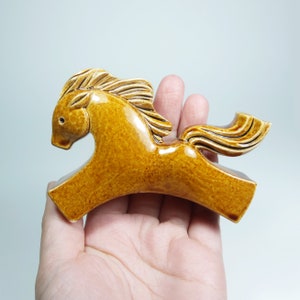May include: A ceramic horse figurine in a brown glaze. The horse is running with its head turned to the side and its tail flowing behind it.
