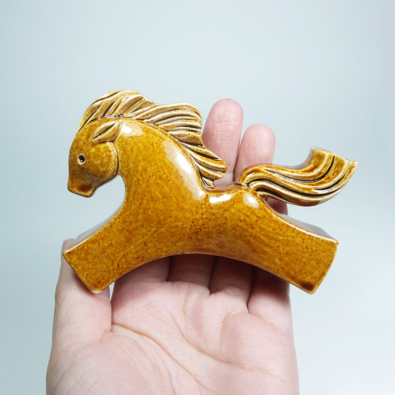 May include: A ceramic horse figurine in a brown glaze. The horse is running with its head turned to the side and its tail flowing behind it.