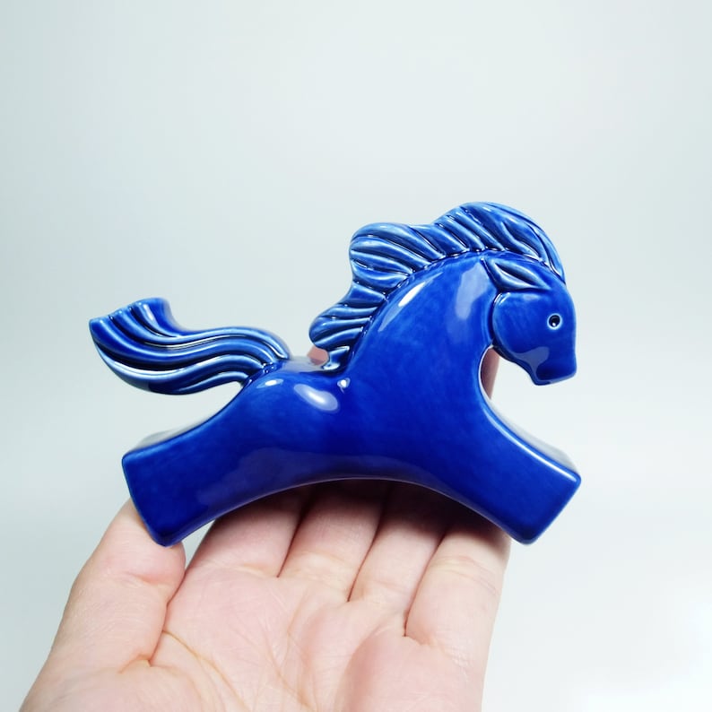 May include: A blue ceramic horse figurine with a flowing mane and tail. The horse is in a running pose with its head turned to the side.