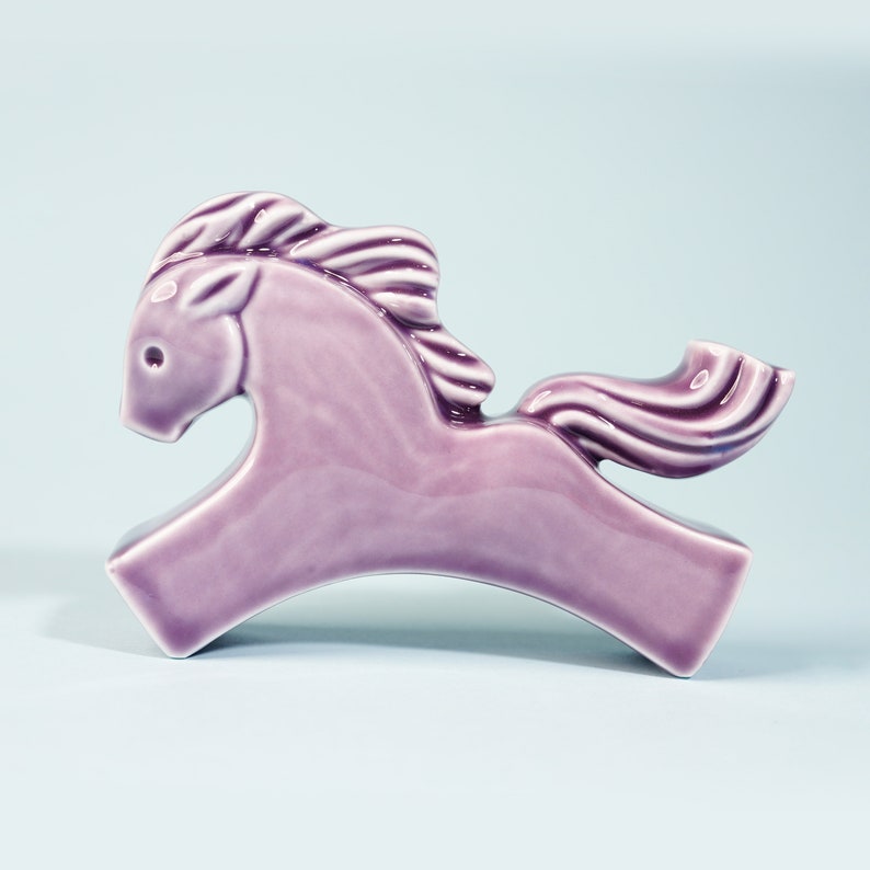 May include: A purple ceramic horse figurine with a stylized mane and tail. The horse is in a running pose with its head turned to the side.
