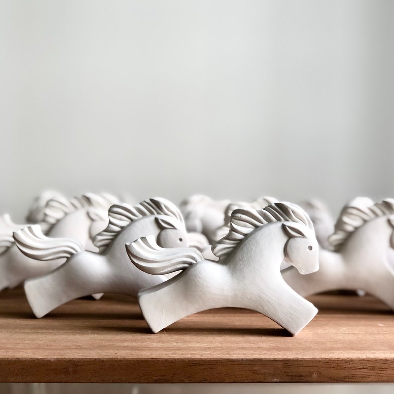 May include: A group of white ceramic horse figurines arranged in a row on a wooden surface. The horses are stylized and have a simple, modern design.