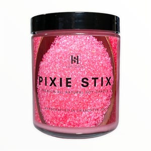 Può includere: Candela di soia rosa in un barattolo di vetro con un coperchio nero. La candela è etichettata "Pixie Stix" e "Premium All Natural Soy Candle". L'etichetta dice anche "Handcrafted in Charlotte, NC".
