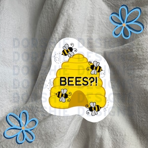 May include: A yellow and black beehive sticker with the text "BEES?!" and five bees around it. The sticker is on a white fabric background.