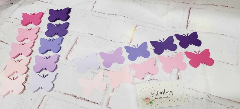 Puede incluir: Una colecci&oacute;n de mariposas de papel en varios tonos de rosa, morado y lavanda. Las mariposas est&aacute;n dispuestas en un patr&oacute;n de degradado, con los tonos m&aacute;s oscuros en la parte superior y los tonos m&aacute;s claros en la parte inferior. Las mariposas son todas del mismo tama&ntilde;o y forma, y tienen un dise&ntilde;o delicado recortado.