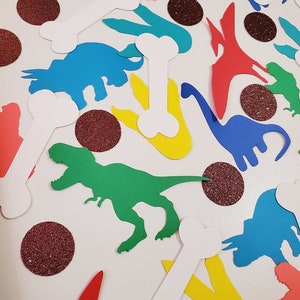 May include: A collection of colorful dinosaur and bone cutouts, perfect for a dinosaur-themed party. The cutouts are made of paper and feature a variety of dinosaurs, including a T-Rex, a Triceratops, and a Stegosaurus. There are also several white bone cutouts.