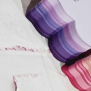 Puede incluir: Una pila de formas de mariposa de papel en capas en tonos de morado, rosa y blanco. Las mariposas est&aacute;n dispuestas en forma de coraz&oacute;n.