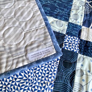 Op de afbeelding: Een blauwe en witte patchworkdeken met een label met de tekst "Handmade by Allyson Lincolnshire, England".