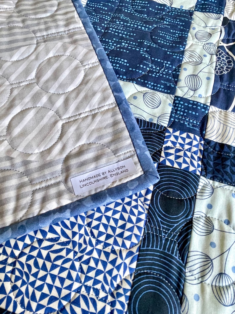 Op de afbeelding: Een blauwe en witte patchworkdeken met een label met de tekst "Handmade by Allyson Lincolnshire, England".