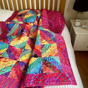 May include: A vibrant patchwork quilt featuring a variety of colourful geometric shapes and intricate patterns in shades of hot pink, bright yellow, electric blue, and deep purple, with a quilted texture and a wide border of pink floral motifs.