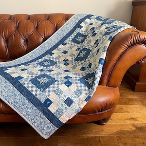 Puede incluir: Una colcha de patchwork con una variedad de patrones de tela en azul y blanco, incluyendo estampados florales, cuadros vichy y cuadrados azul marino sólidos. La colcha tiene un borde ancho con diseño de enredadera y acolchado.