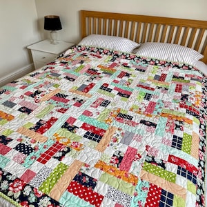 May include: A colorful patchwork quilt with a variety of patterned fabrics, including floral, polka dot, and striped designs. The quilt features a white background and is bordered with a dark floral fabric. The quilt is on a bed with striped pillows.