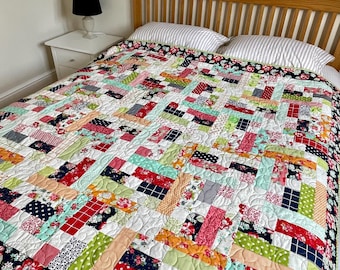 May include: A colorful patchwork quilt with a variety of patterned fabrics, including floral, polka dot, and striped designs. The quilt features a white background and is bordered with a dark floral fabric. The quilt is on a bed with striped pillows.