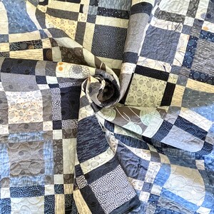 Op de afbeelding: Een blauwe en witte quilt met een geometrisch patroon. De quilt is gemaakt van verschillende stoffen met verschillende texturen en ontwerpen. De quilt is spiraalvormig gevouwen.