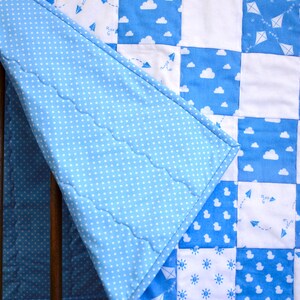 May include: A blue and white baby quilt with a patchwork design featuring clouds, airplanes, and suns. The quilt is made of soft cotton fabric and is perfect for a nursery or crib.