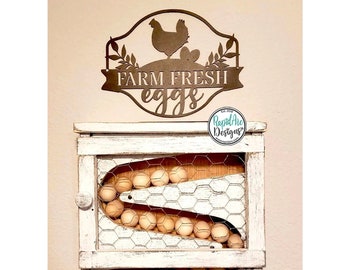 May include: White wooden egg holder with a wire mesh front and a metal sign that reads "Farm Fresh Eggs" with a silhouette of a chicken. The holder has a sliding door and a shelf for storing eggs.