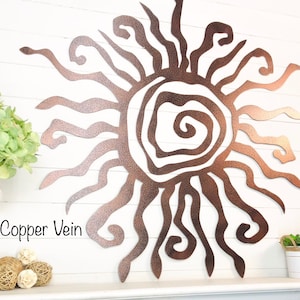 May include: A copper vein metal sunburst wall art piece. The sun design features a textured finish and a swirling centre. The text "Copper Vein" is visible in the image. The sun's rays extend outwards in various shapes.