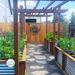 May include: A garden pathway with raised beds, a wooden pergola, and a wooden fence. The pathway is made of stepping stones. A metal sun design is mounted on the wooden fence. The raised beds are filled with various plants. The sky is blue with some clouds.