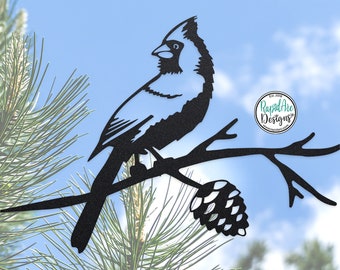 May include: Black metal silhouette of a cardinal perched on a branch with a pine cone. The silhouette is against a blue sky background.