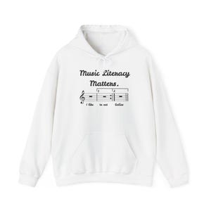 May include: A white hooded sweatshirt featuring black text that reads Music Literacy Matters. Below the text is a musical staff with a treble clef, repeat signs, and the words I like to eat babies printed in a cursive font underneath the staff.